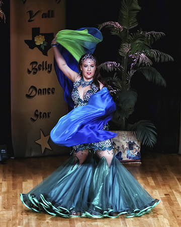 dancer in ornate blue and green costume with coordinating headpiece spins with a blue and green silk veil