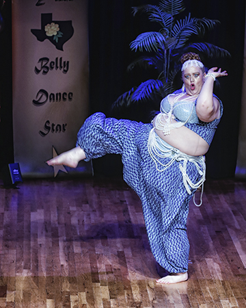 dancer in blue and white costume with pants and beads kicking right foot forward