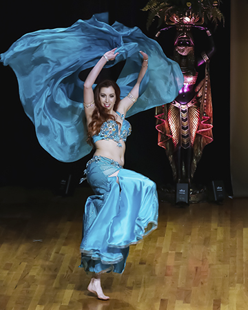 dancer wearing a turquoise blue dramatically lifts her matching silk veil behind her as shie raises a knee during a level change