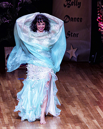dancer wearing white and pale ice blue wraps herself in coordinating veil while smiling at the audience