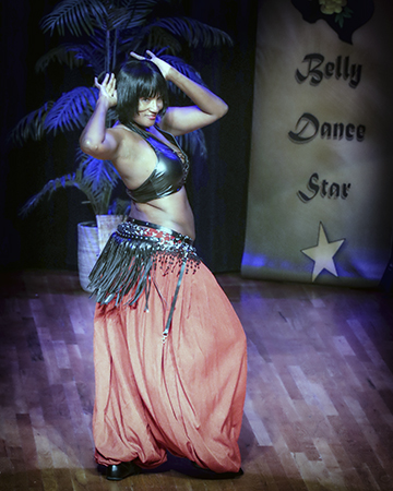 dancer wearing earthy orange-colored full pants twists toward audience with her hands placed behind her head