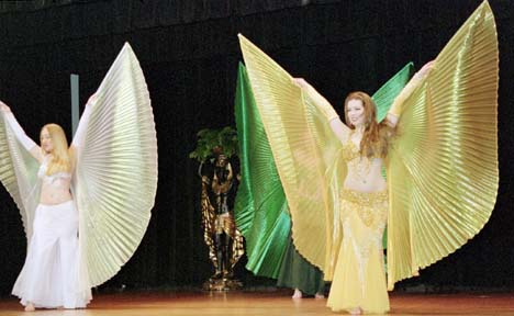 3 dancers with wings outstretched perform in white, green, and gold