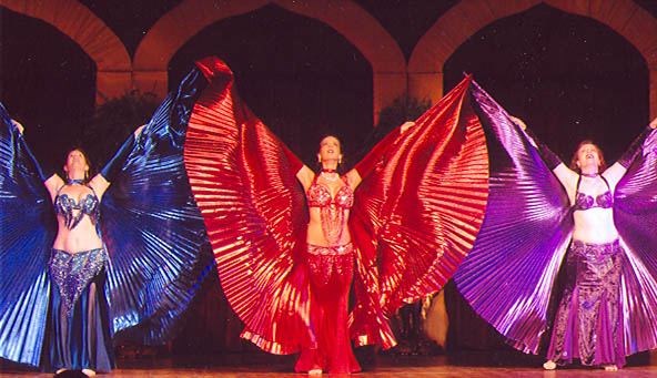 3 dancers wearing blue, red, and purple looking up with isis wings outstretched in a v-shape