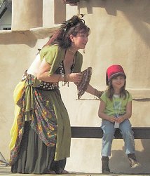 dancer wearing green and holding a fan in her hand bends down next to young audience member who has been asked to sit on stage during show