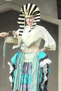 dancer wearing a multi-colored costume and wearing a large egyptian-styled hat stands on stage while holding a small basket