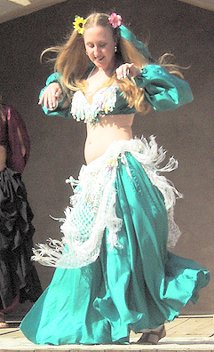 dancer wearing green with white and flowers in her hair performing on stage in the sunshine