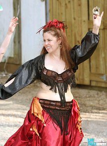 dancer with red feathers in her hair, wearing a red and black costume, plays zills during a performance