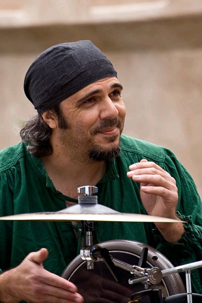 drummer wearing a black head wrap and green shirt plays drum with cymbal shown in foreground