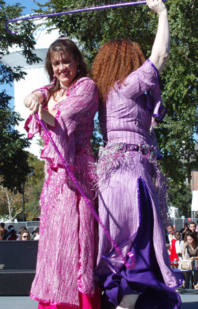2 dancers wearing pink and purple perform with canes while standing back to back