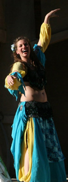 dancer wearing a turquoise and yellow costume with black bedlah laughs on stage during performance