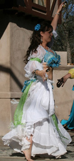 dancer wearing a white costume with turquoise and lime green accents performs and plays zills on stage