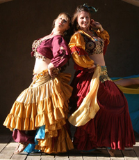 2 dancers wearing orange and yellow pose on stage, standing back to back