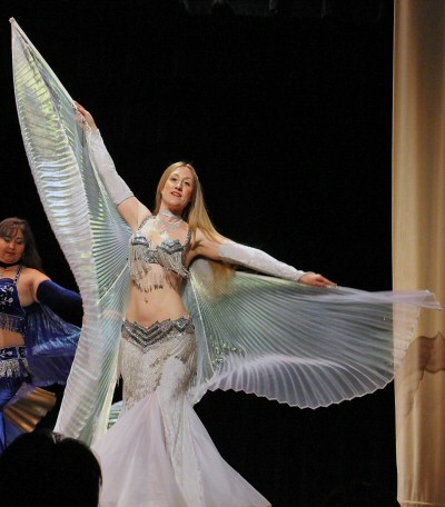 dancer performing with white wings in an all white costume with silver bedlah