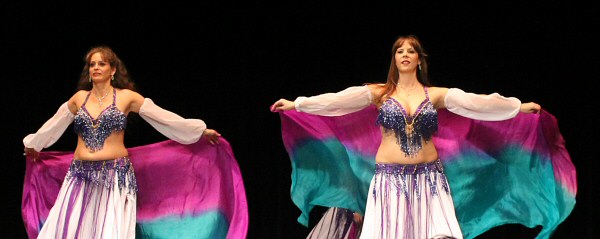 2 dancers wearing white sleeves and skirts and purple bedlah perform with colorful veils