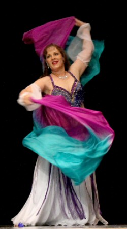 dancer wearing white costume and purple bedlah swirls a colorful veil around her while smiling during performance