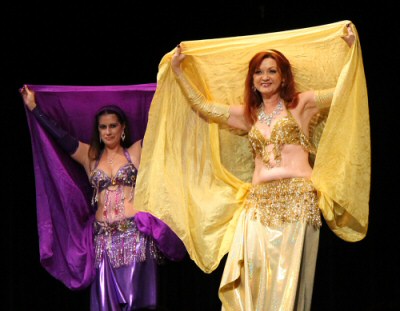 2 dancers wering purple and gold smile at audience while performing using matching veils