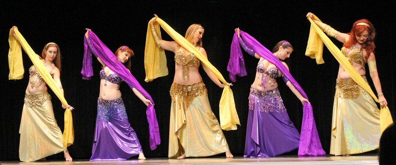 5 dancers perform on stage with veils, wearing alternating gold and purple