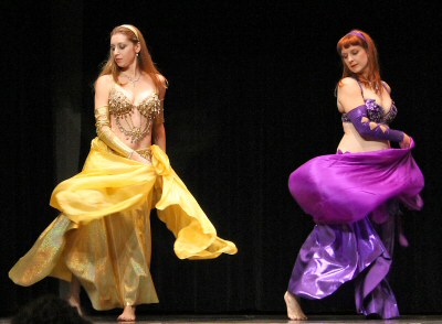 2 dancers wering purple and gold look downward while performing using matching veils
