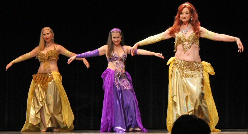 3 dancers perform on stage wearing alternating gold and purple