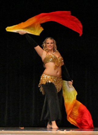 dancer performs on stage wearing black costume and gold bedlah with fire-toned fan veils
