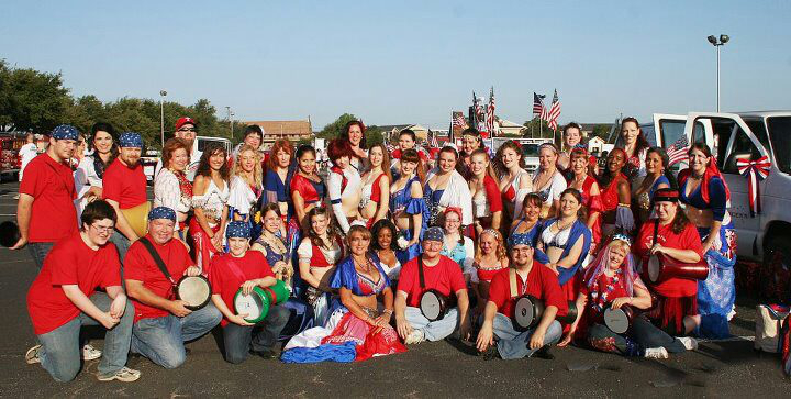 a large group of dancers and drummers wearing red, white, and blue poses for a photo while waiting for the parade to begin
