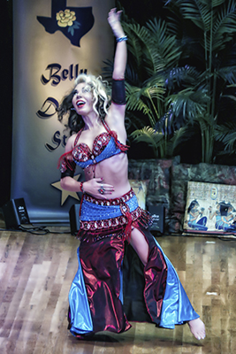  dancer wearing a metallic red and blue costume smiles with one arm outstretched above her