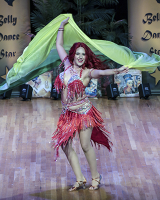 dancer in a fringe covered red and silver costume with a knee length skirt spins with a yellow and sage green veil