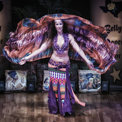 dancer wearing earthy purple and orange costume dances with a veil floating behind her and facing the audience
