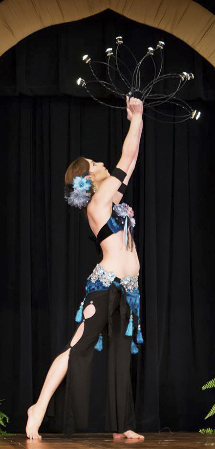 dancer wearing black pants and costume with blue accents holding candles